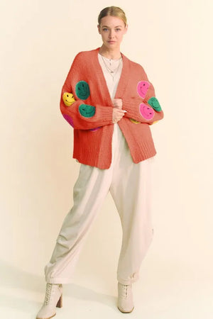 Woman wearing a colorful cardigan with floral patterns on a plain background