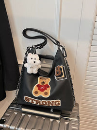 Black handbag with teddy bear and 'STRONG' patch on a silver suitcase.