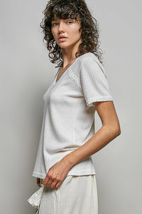 Woman wearing a light gray textured top and white pants against a plain background