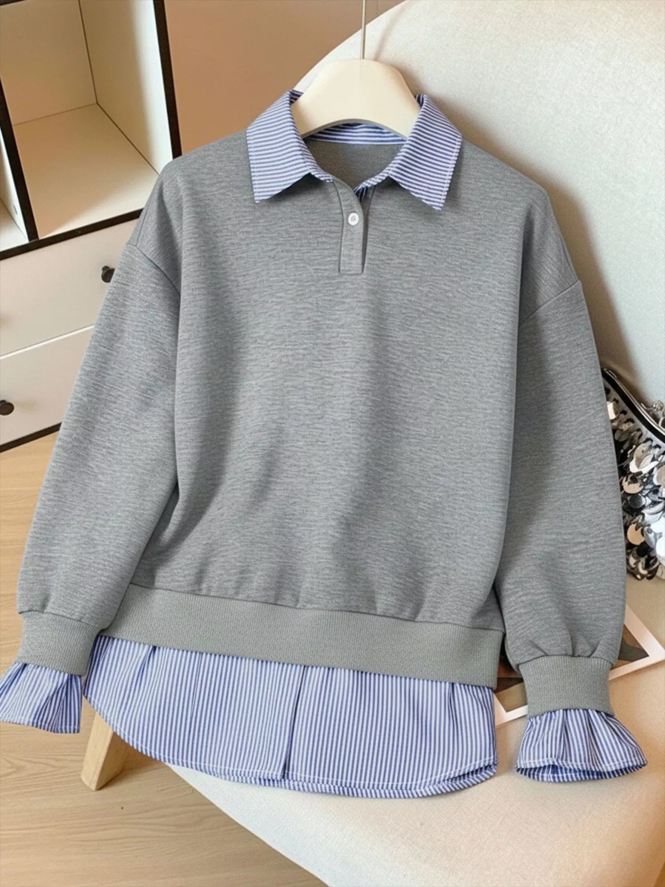 Gray sweatshirt with blue striped collar and hem on a mannequin against a neutral background