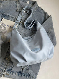 Light blue handbag on a denim jacket with a glass of water and a book in the background.