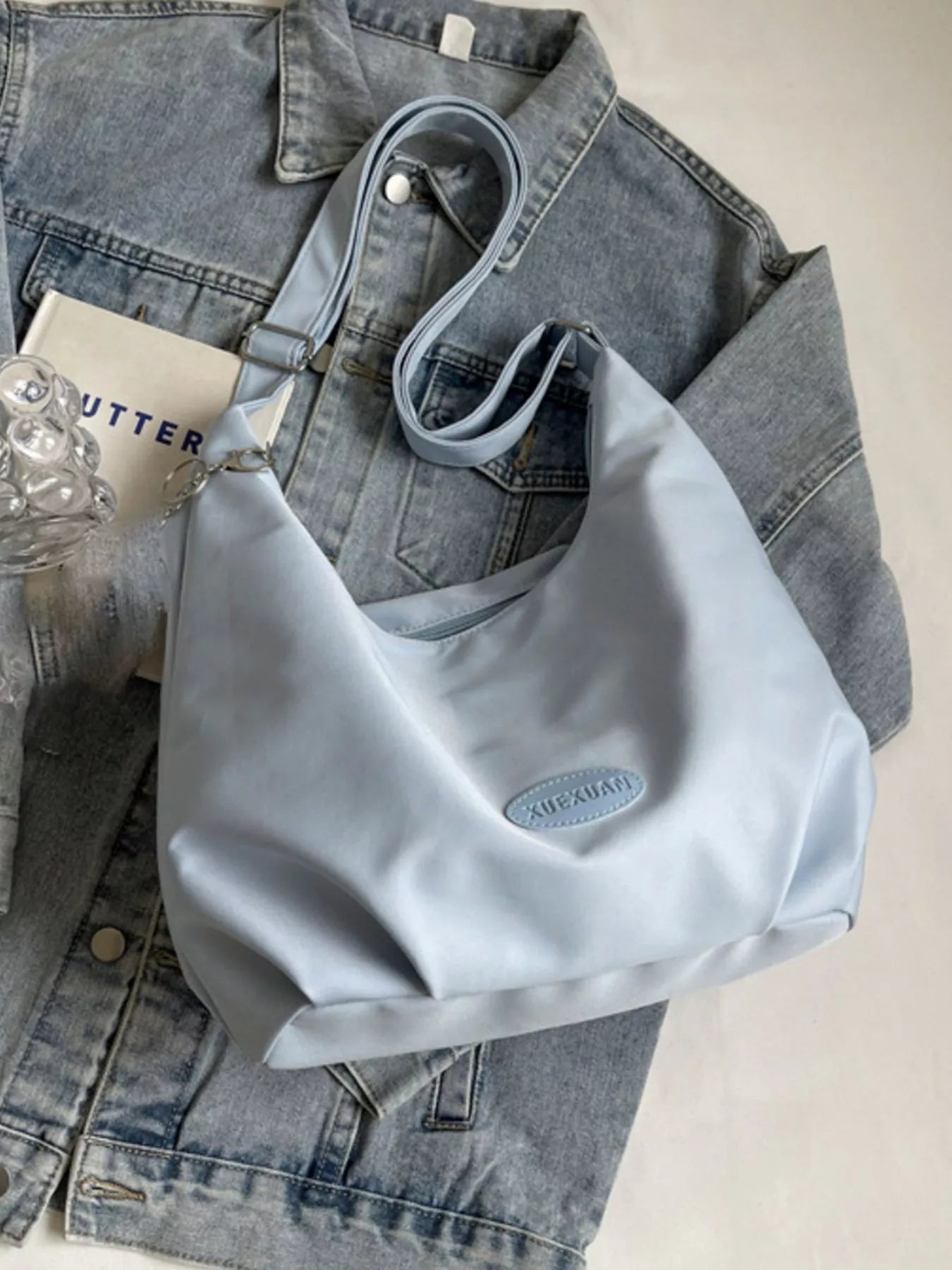 Light blue handbag on a denim jacket with a glass of water and a book in the background.