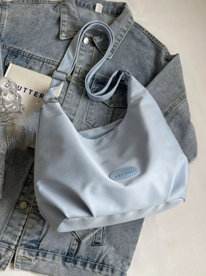Light blue handbag on a denim jacket with a glass of water and a book in the background.