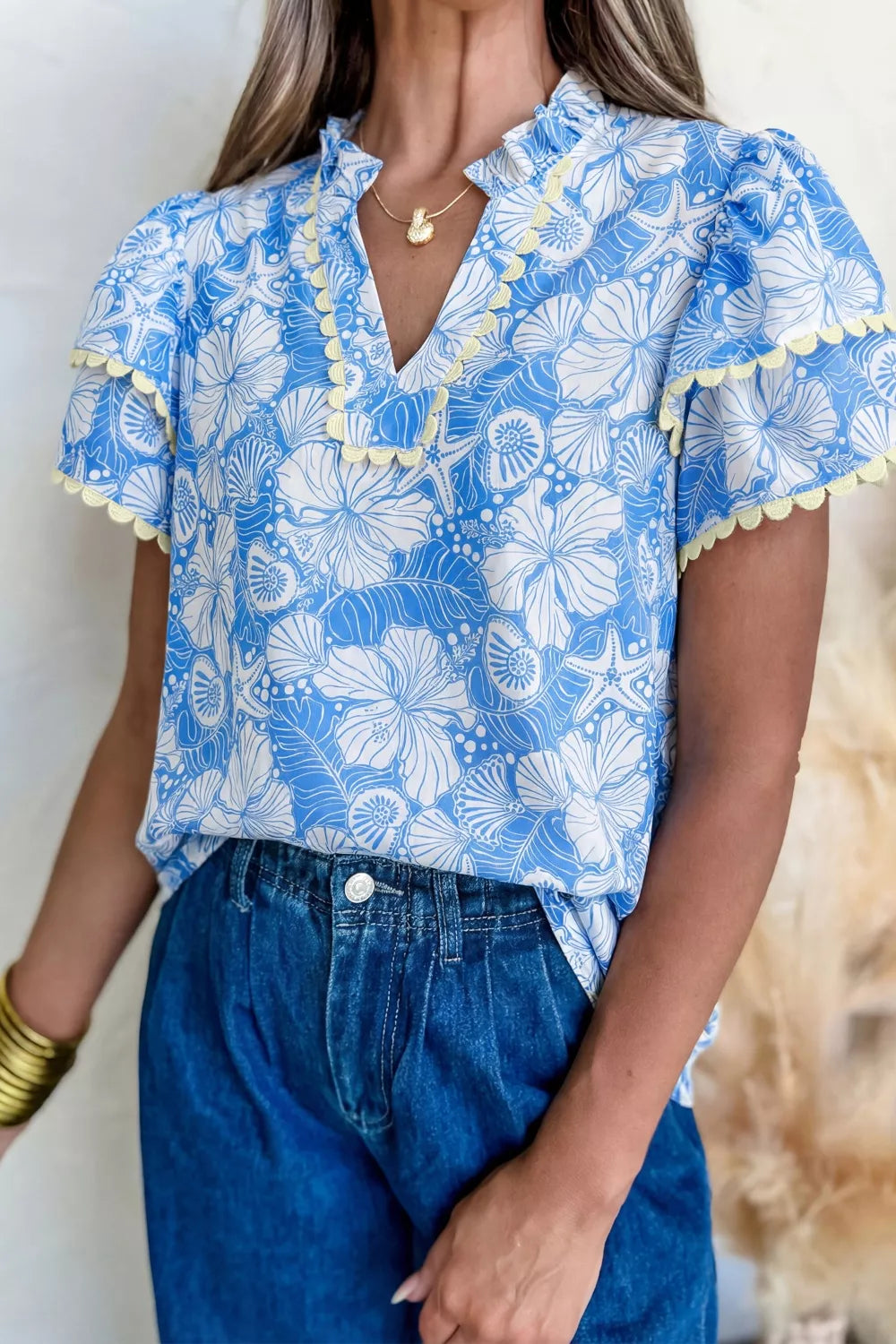 Woman wearing a blue floral blouse with ruffled sleeves and denim pants.