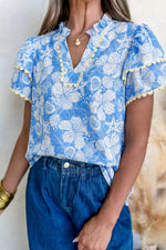 Woman wearing a blue floral blouse with ruffled sleeves and denim pants.