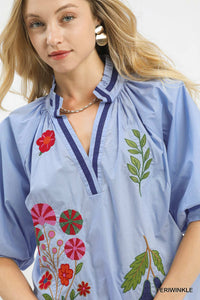 Woman wearing a light blue blouse with floral and leaf embroidery on a white background