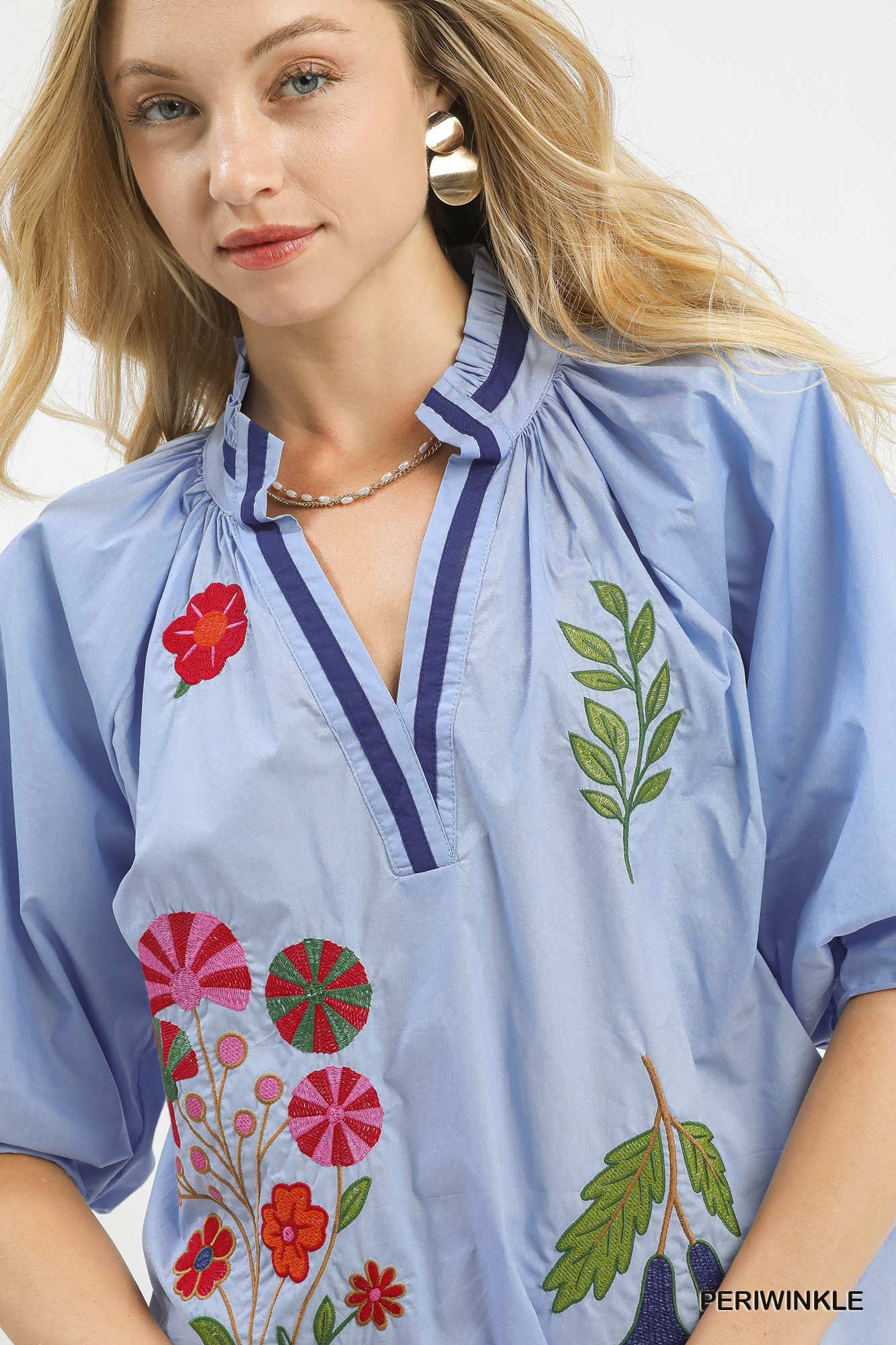 Woman wearing a light blue blouse with floral and leaf embroidery on a white background