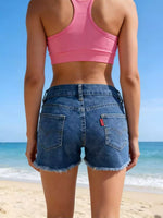 Person wearing a pink sports bra and blue denim shorts on a beach.