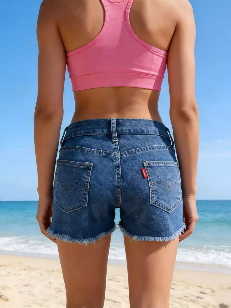 Person wearing a pink sports bra and blue denim shorts on a beach.