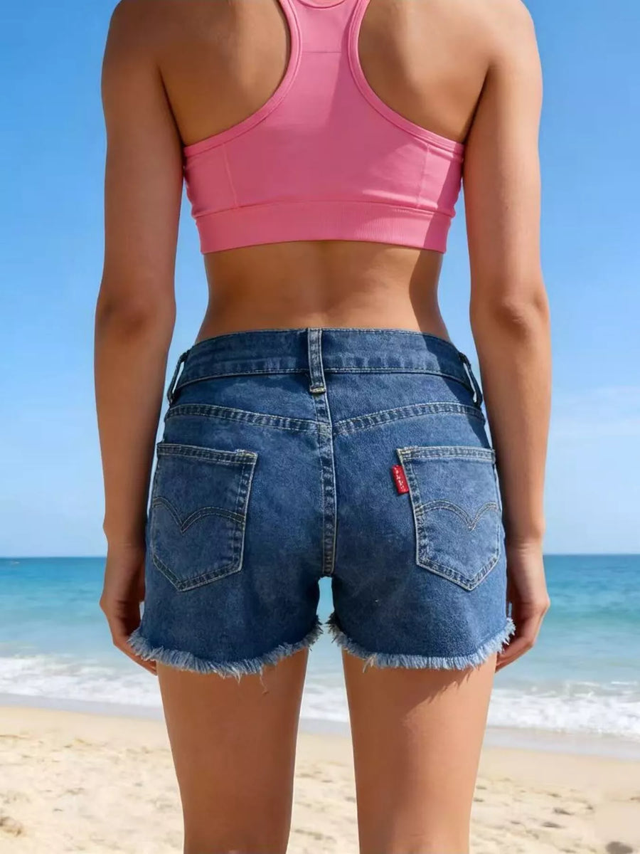 Person wearing a pink sports bra and blue denim shorts on a beach.