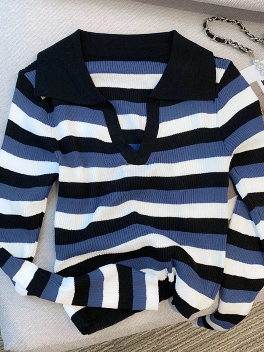 A long-sleeve ribbed knit polo sweater with horizontal stripes in navy blue, black, and white, featuring a solid black collar, laid flat on a light beige fabric surface.