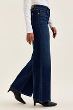 Person wearing dark blue flared jeans on a beige background
