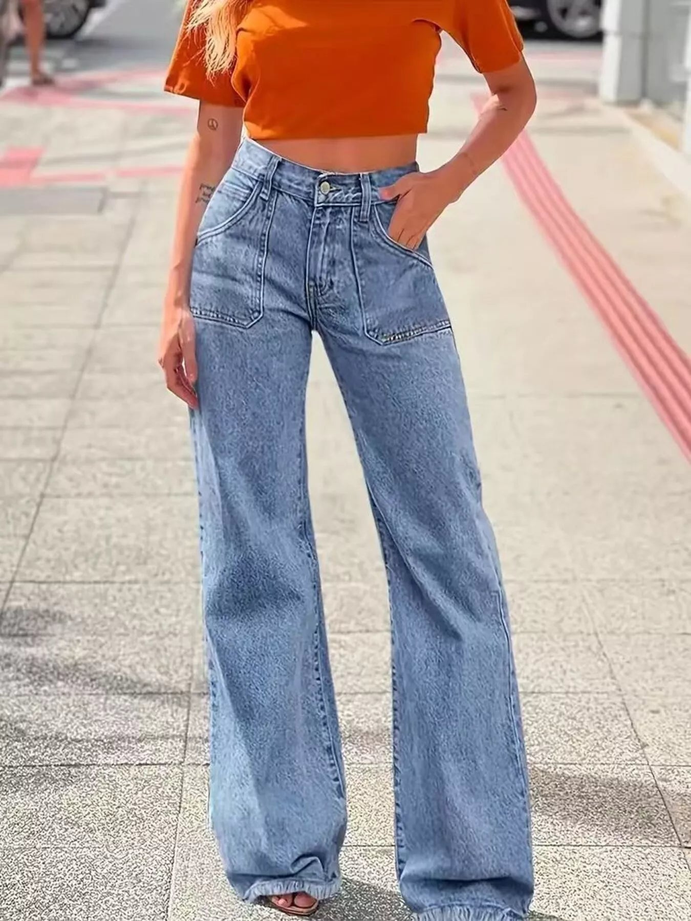 Person wearing an orange crop top and blue jeans on a sidewalk.