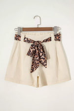Beige shorts with a leopard print belt on a hanger against a white background