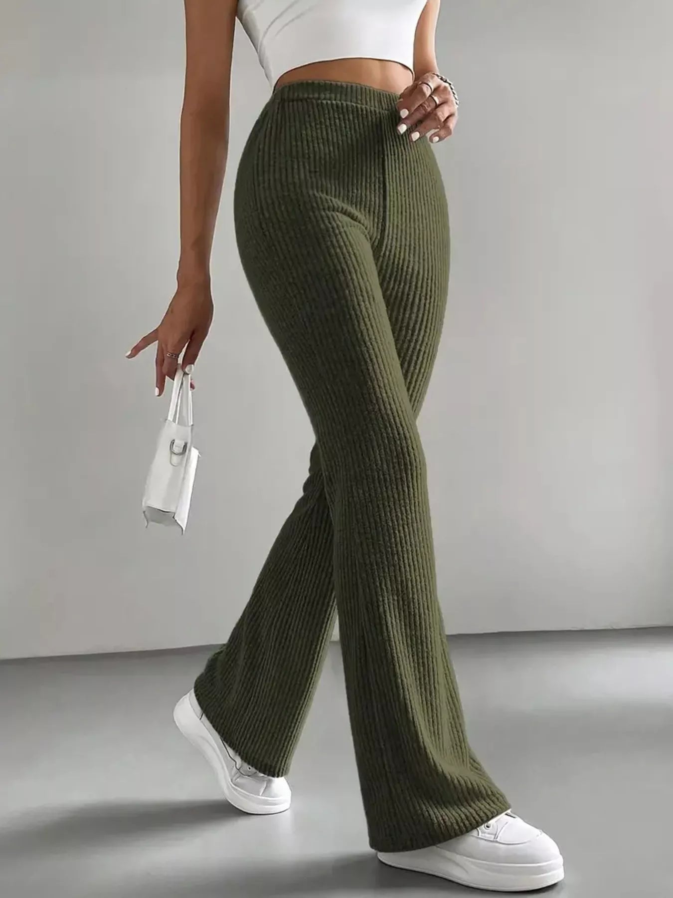 Person wearing olive green ribbed pants and white sneakers on a gray background