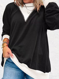 Person wearing a black and white ribbed sweater with a plain background