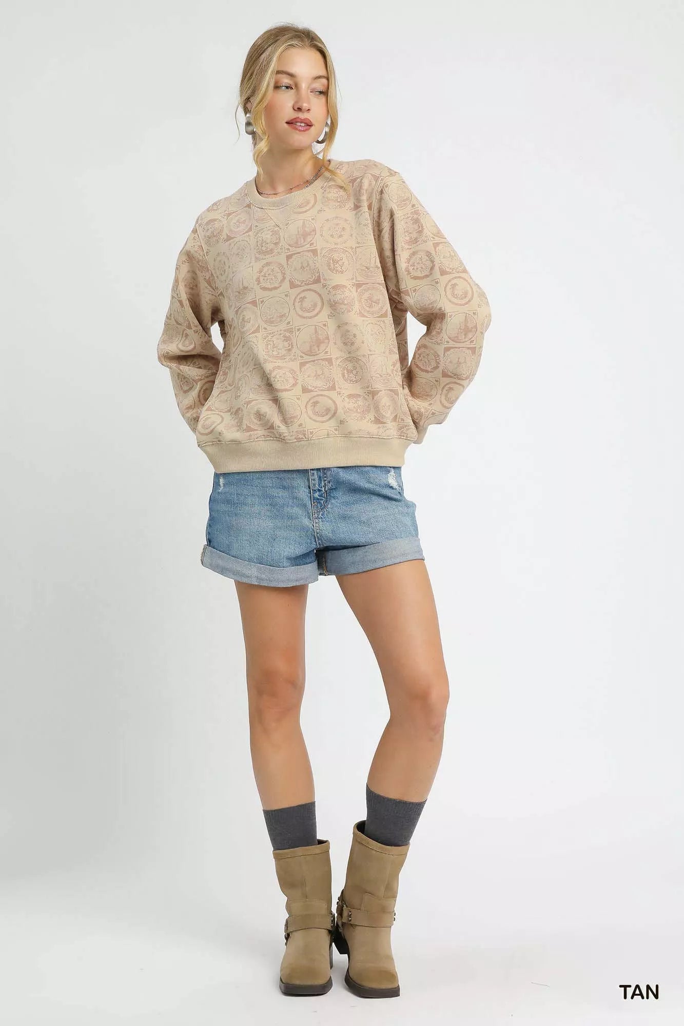 Woman wearing a beige textured sweater, denim shorts, and brown boots on a white background