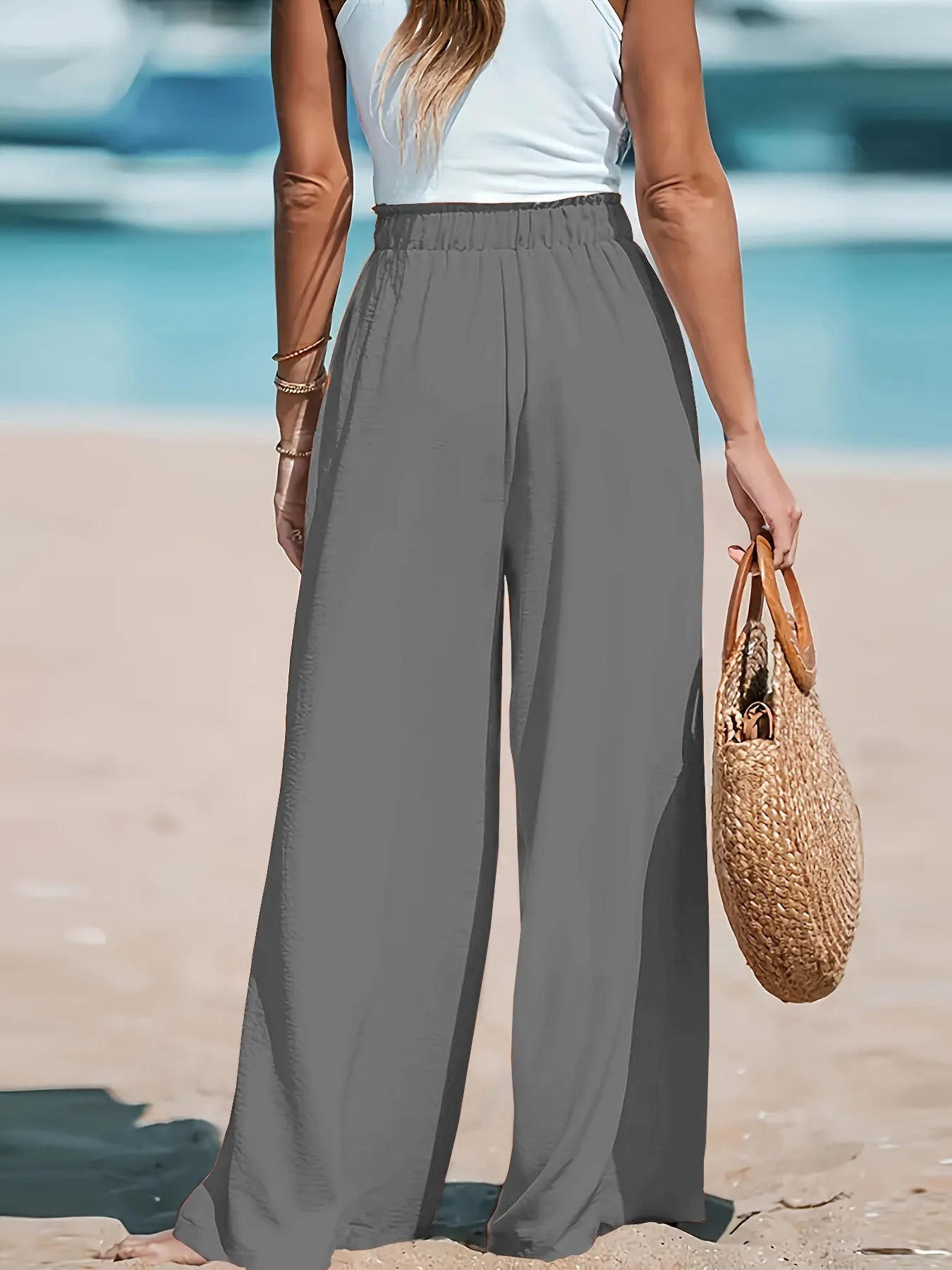Person wearing gray wide-leg pants and a white top on a beach.