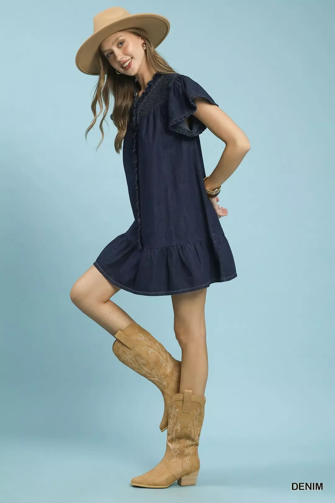 Woman wearing a navy dress and tan boots with a blue background