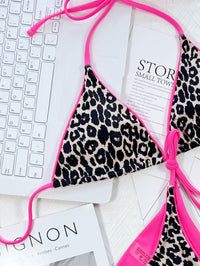 Leopard print bikini top with pink straps on a white surface with text and keyboard.