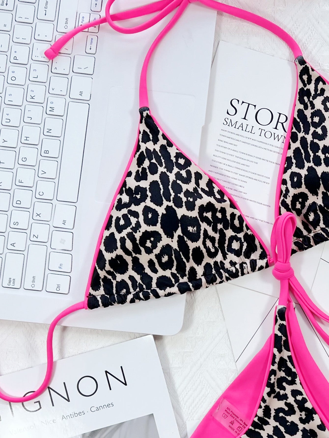Leopard print bikini top with pink straps on a white surface with text and keyboard.