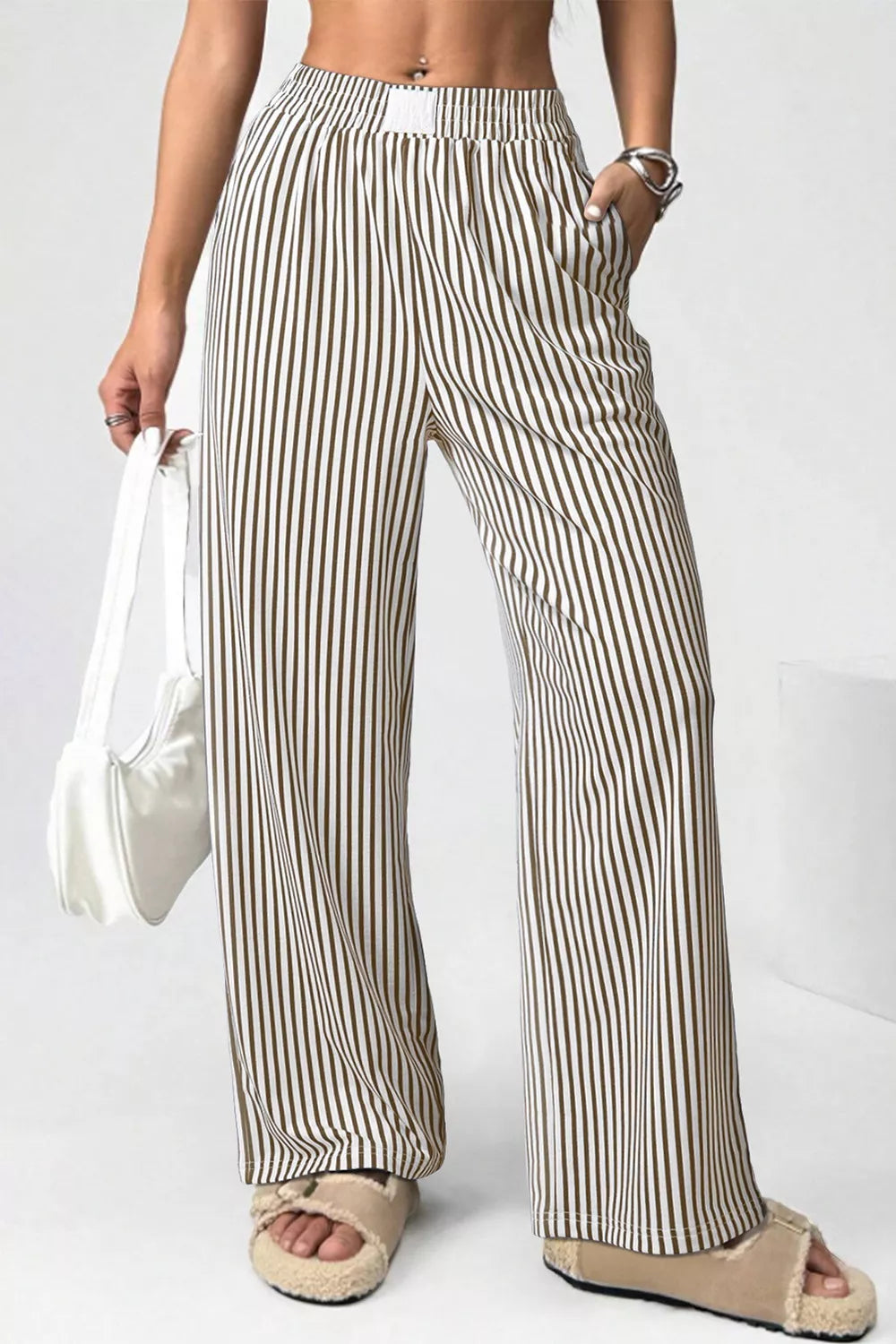 Person wearing striped pants holding a white bag on a plain background