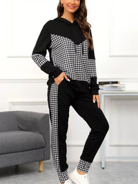 Woman wearing a black and white houndstooth patterned tracksuit in a room with a gray sofa and white wall.