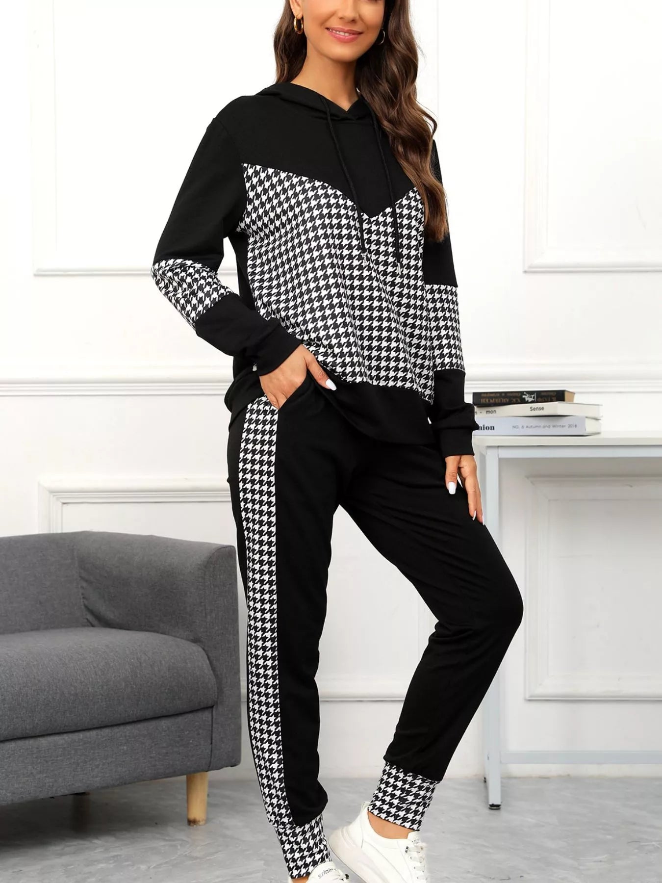 Woman wearing a black and white houndstooth patterned tracksuit in a room with a gray sofa and white wall.