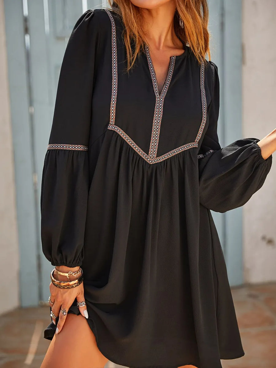 Black dress with intricate detailing worn by a person, standing against a neutral background.