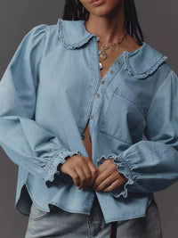 Person wearing a light blue denim shirt with ruffled collar and cuffs against a gray background