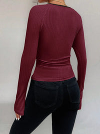 Person wearing a maroon ribbed long-sleeve top and black pants on a plain background