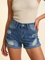 Person wearing distressed blue denim shorts on a beige background