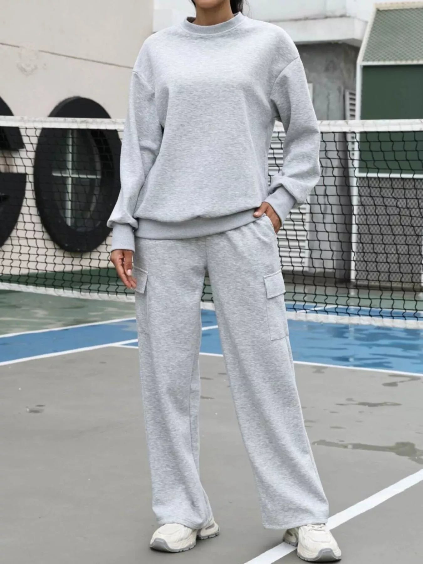 Person wearing a gray sweatshirt and pants on a tennis court