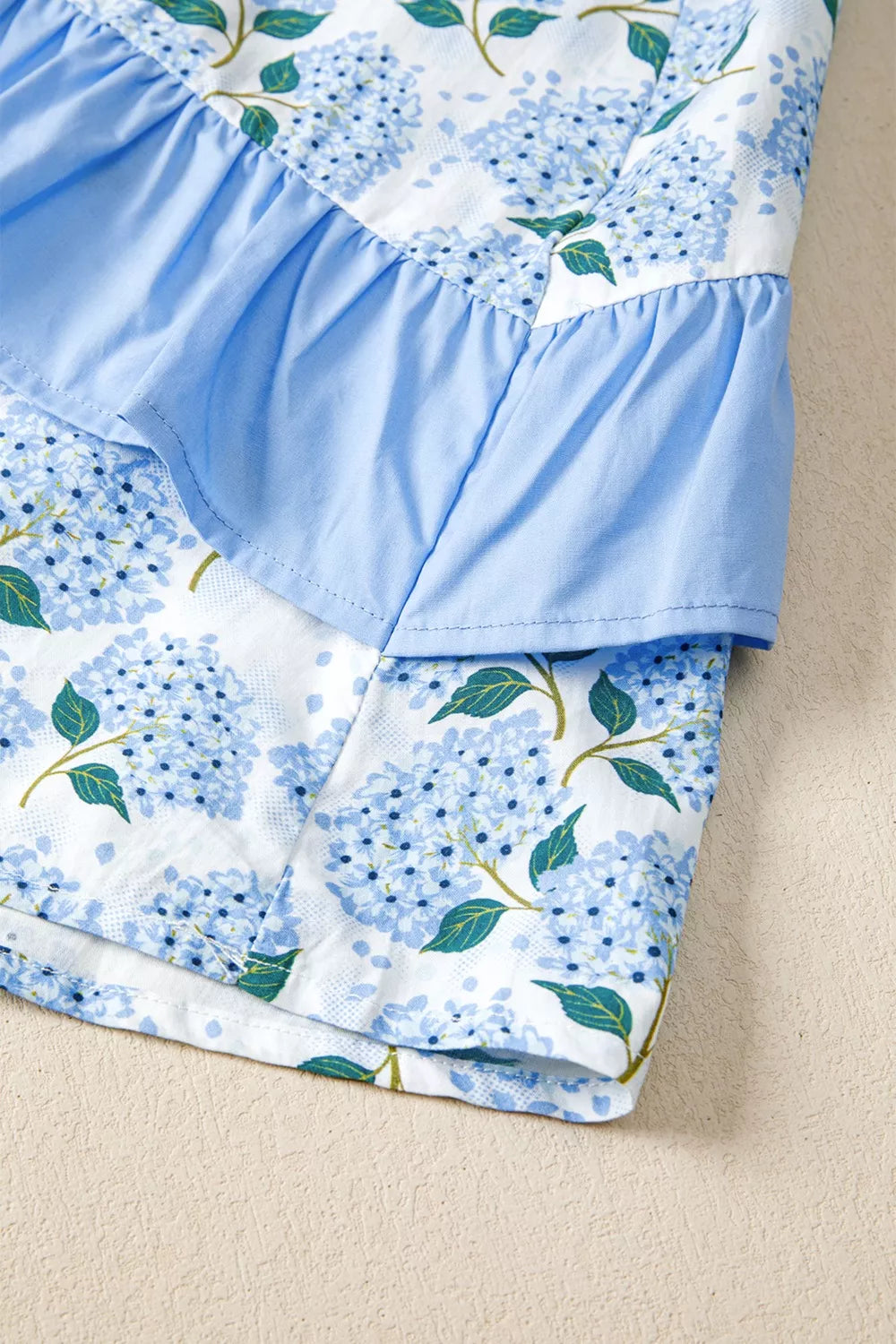 Close-up of a blue floral dress with ruffled layers on a beige background