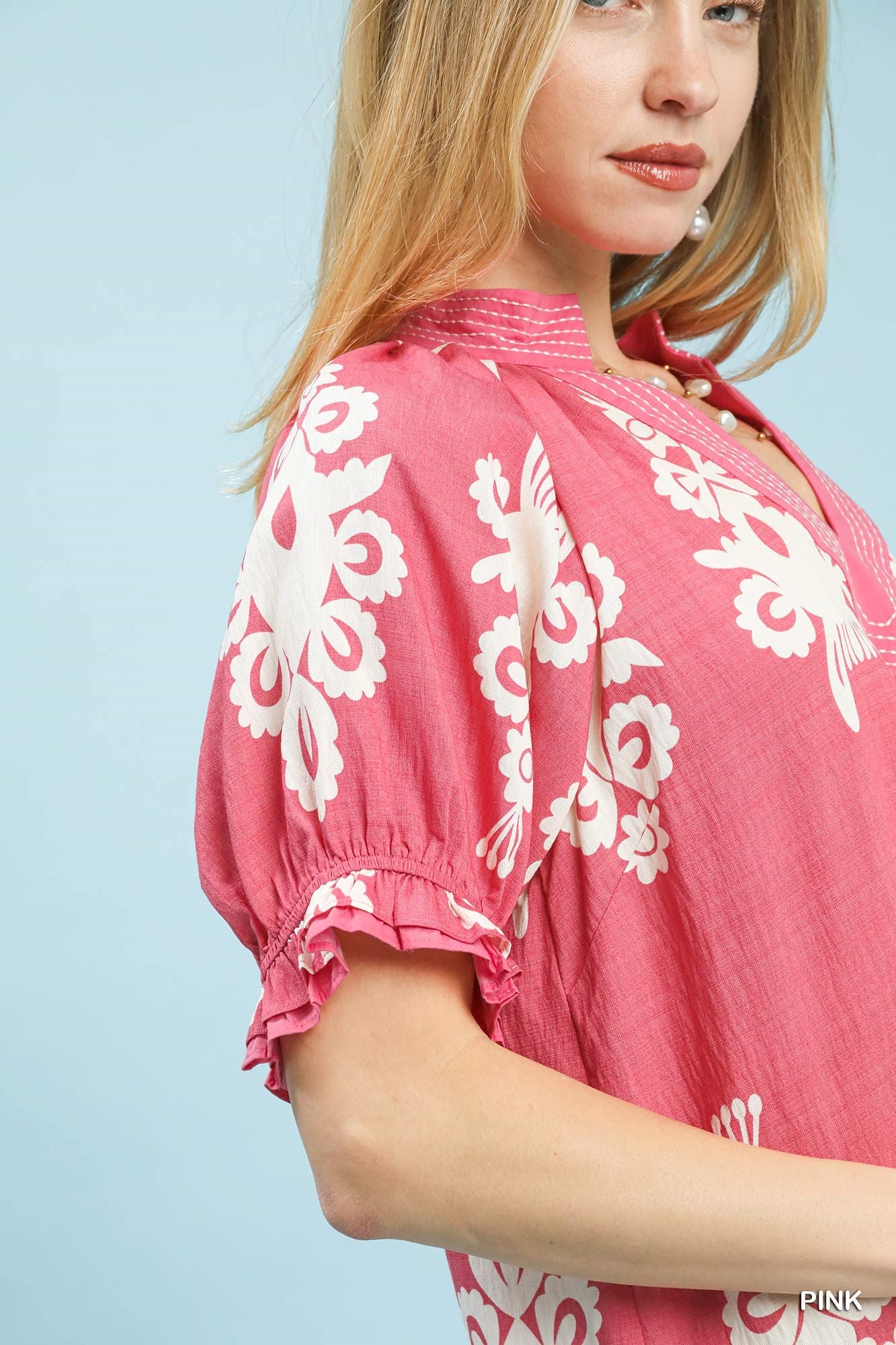 Woman wearing a pink dress with white floral embroidery against a light blue background