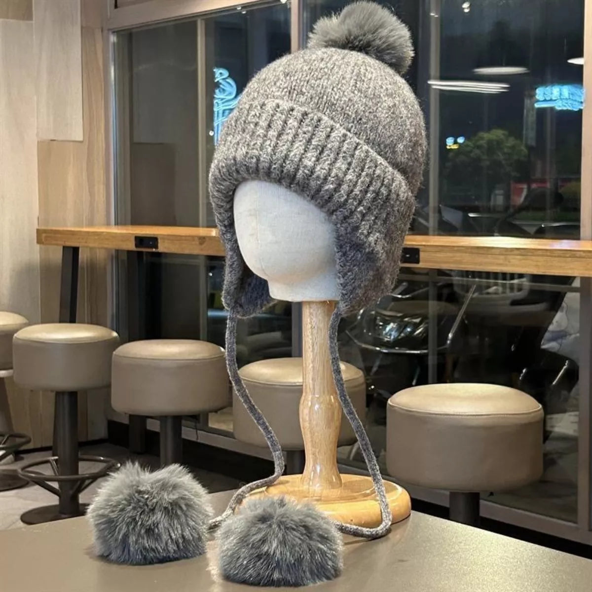 Gray knitted hat with pom-poms on a mannequin head in a restaurant setting