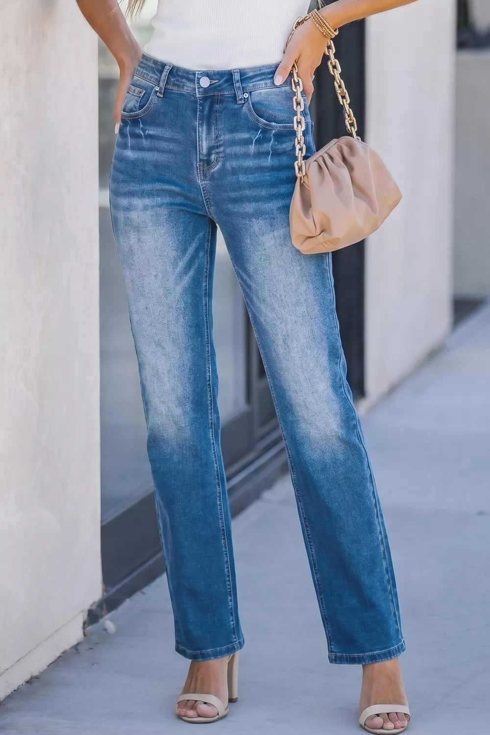 Person wearing blue jeans and a beige handbag on a sidewalk.