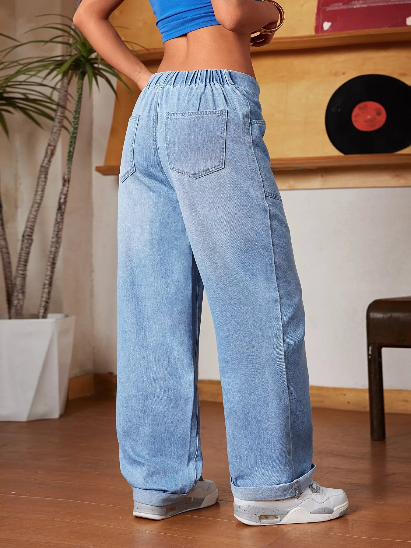 Person wearing light blue jeans in a room with a plant and wooden shelf.