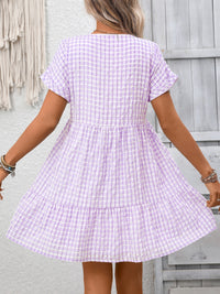 Woman wearing a purple checkered dress against a light gray wall.