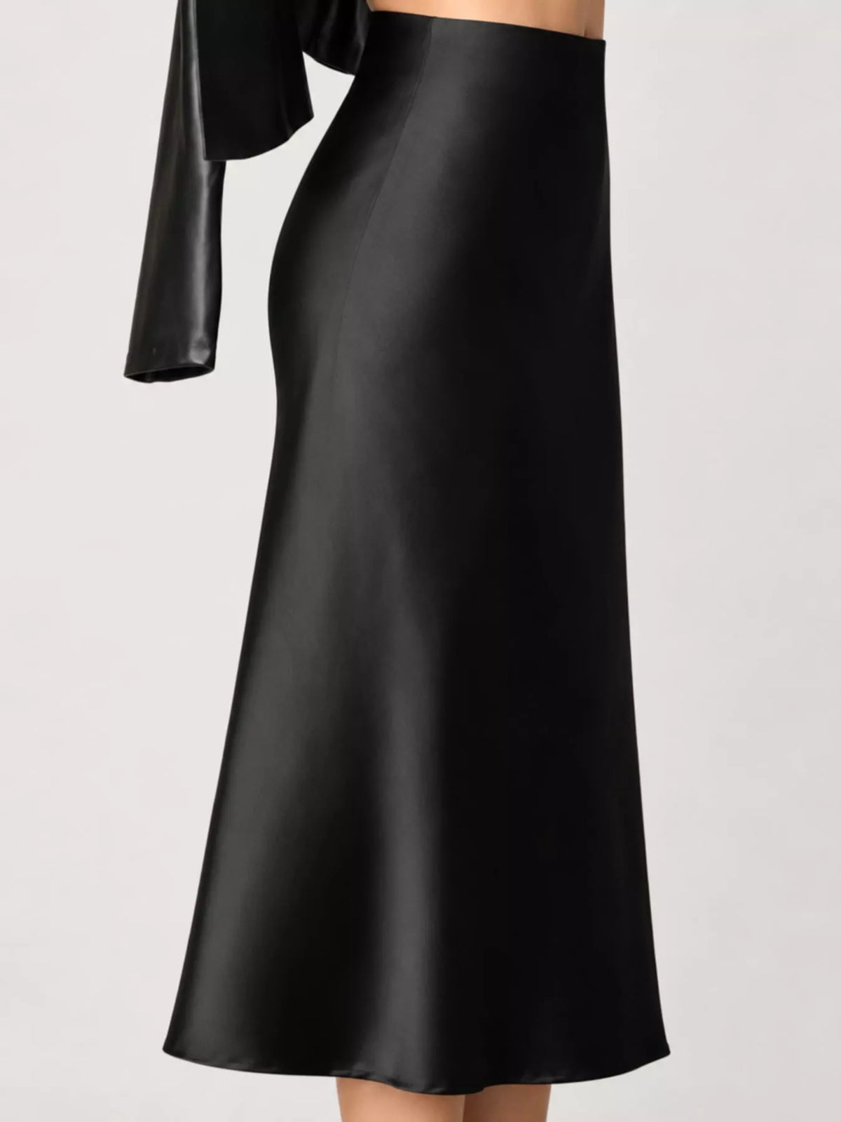 A black satin midi skirt with a high waist and flared silhouette, shown on a model against a light gray studio background.