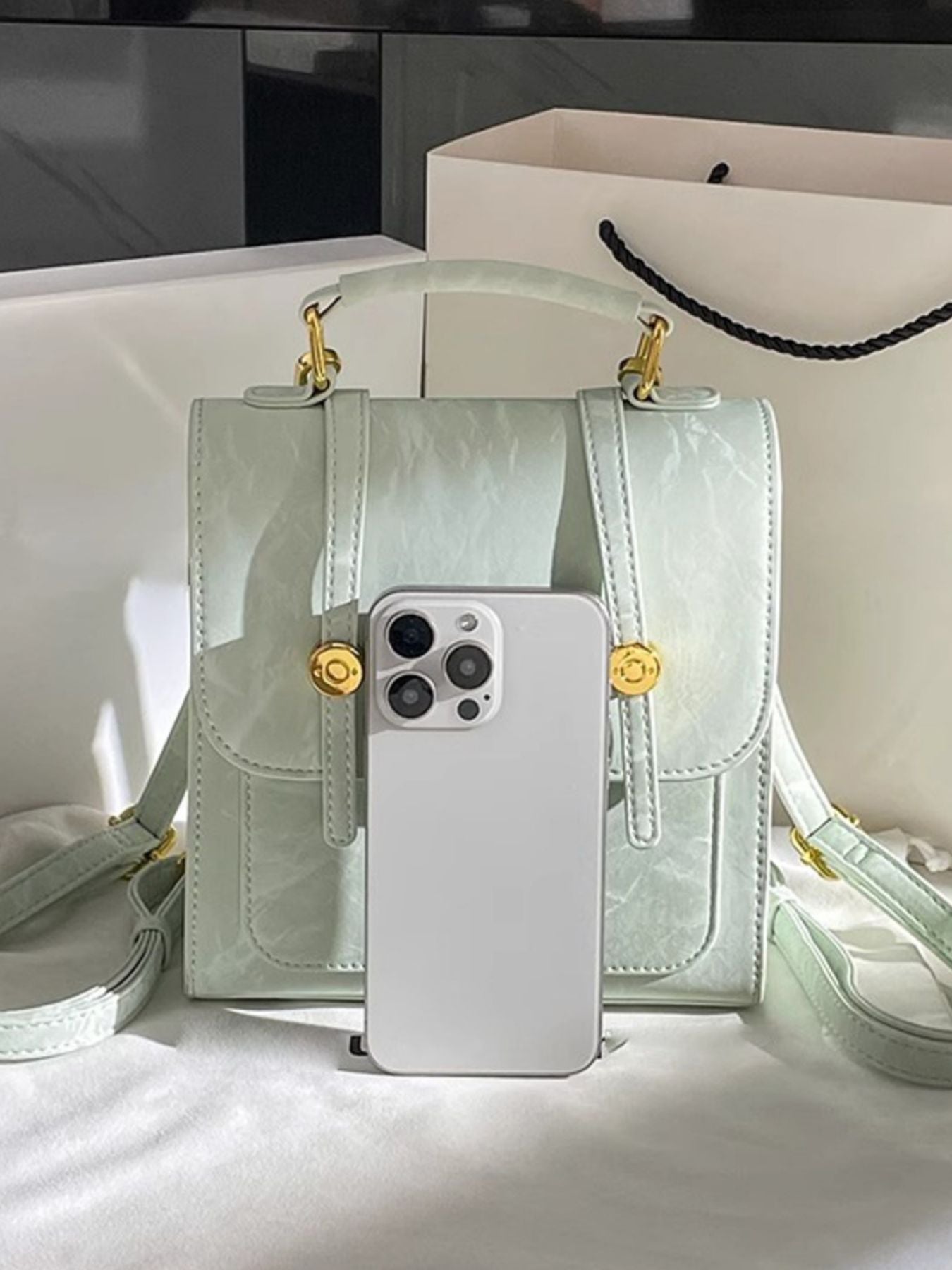 Light green handbag with gold accents and a phone case on a white surface
