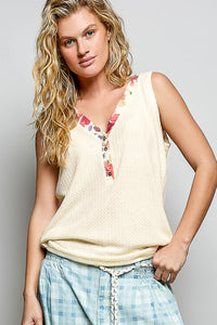 Woman wearing a sleeveless top with floral accents and plaid pants against a plain background
