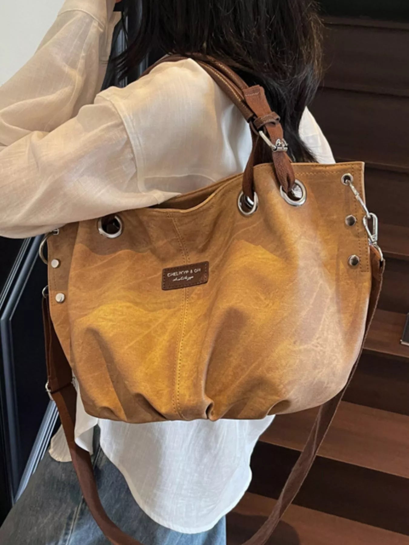 Brown leather handbag with visible brand name held by a person.