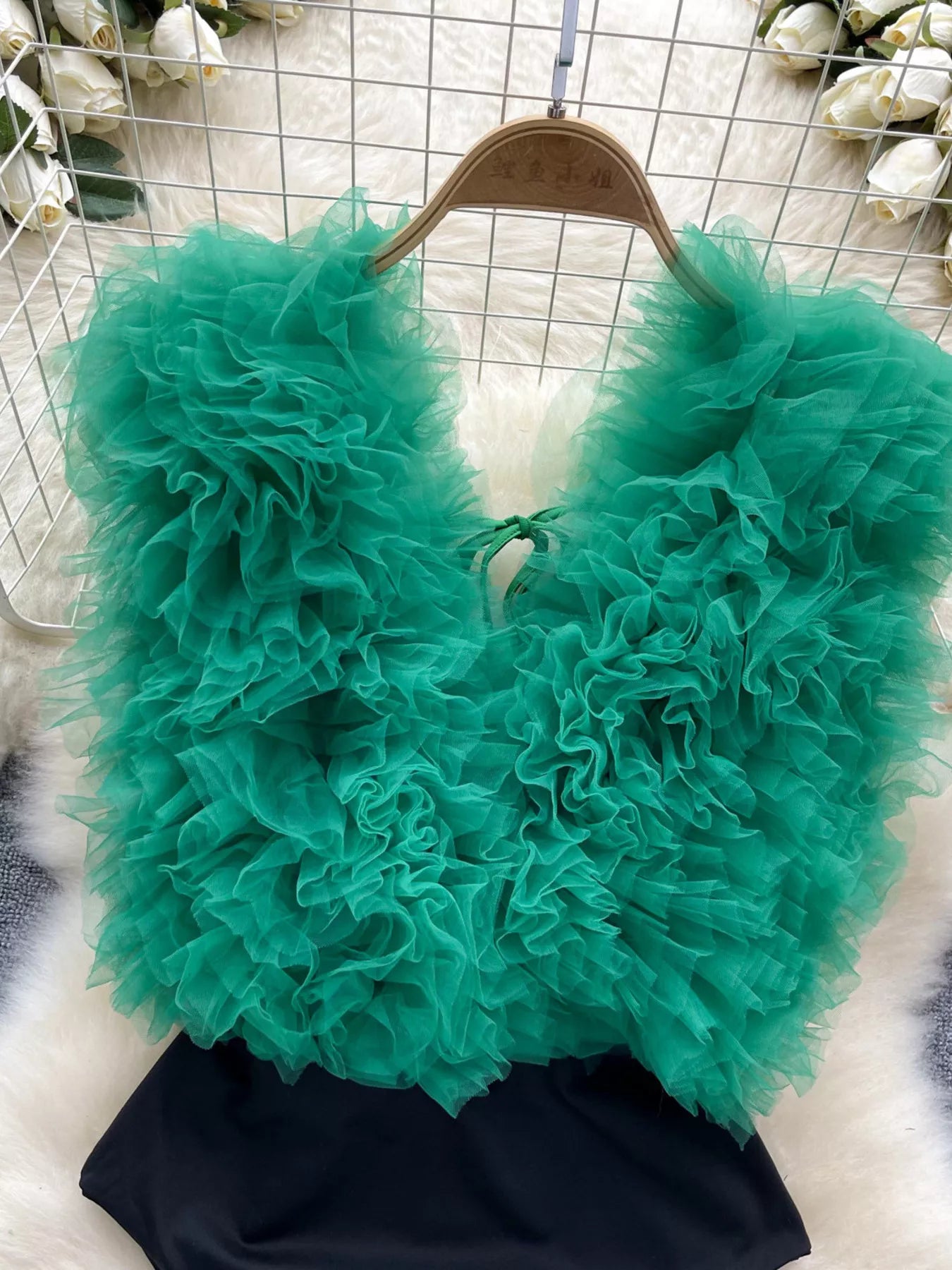 Teal ruffled top on a hanger with a floral background