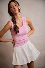 Woman wearing a pink top and white skirt against a plain background