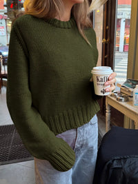 Person wearing a green sweater holding a coffee cup in an indoor setting.