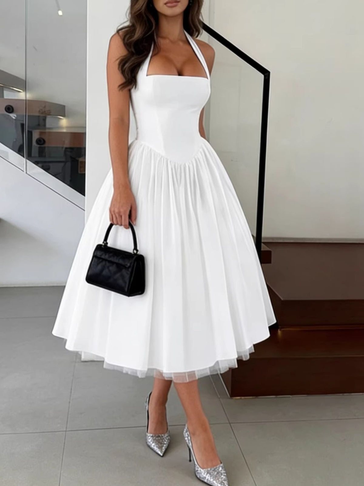 Woman wearing a white halter neck dress with a black handbag indoors.