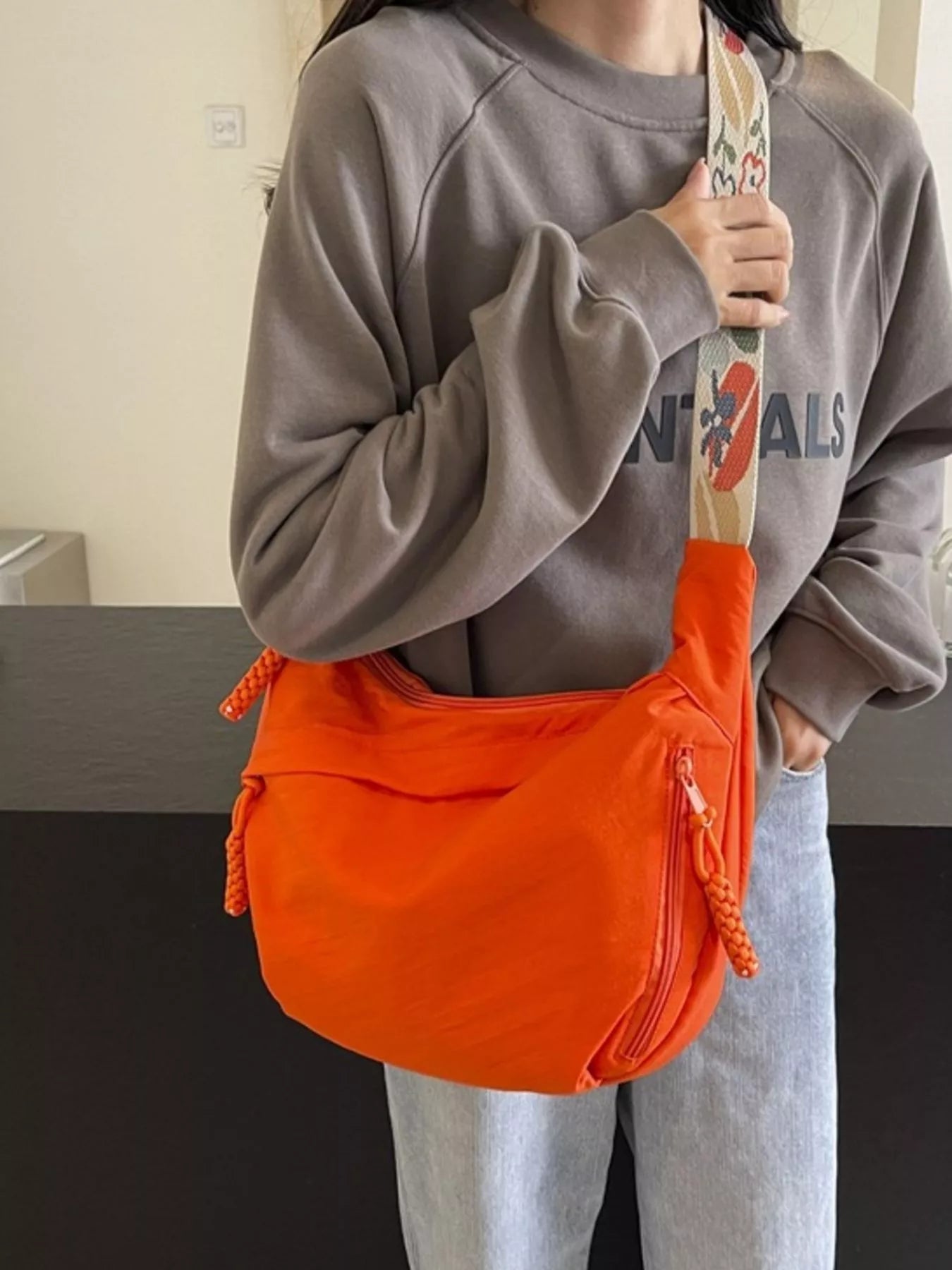 Person wearing a gray sweatshirt and light blue jeans, holding an orange bag with a colorful design.