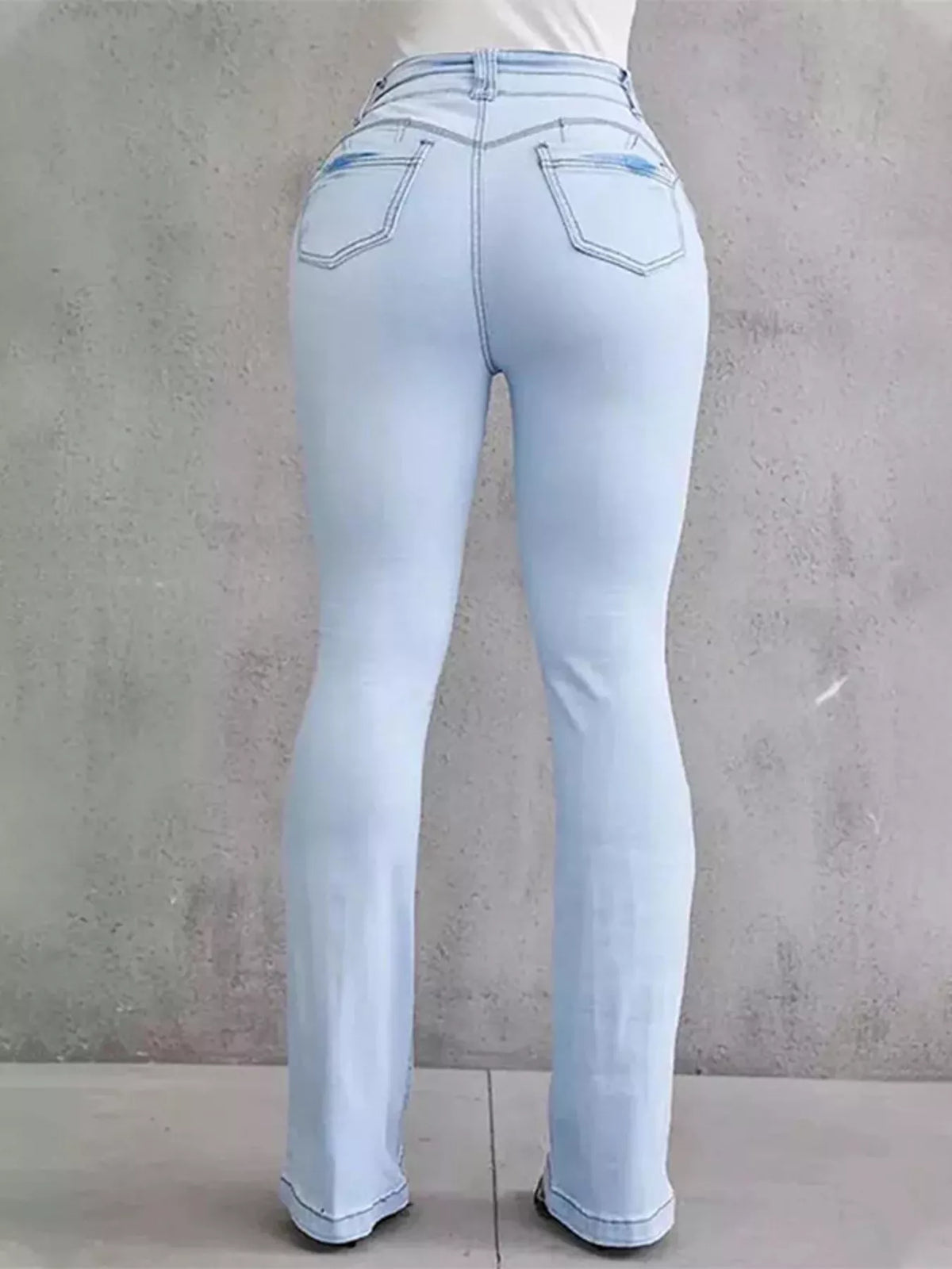 Light blue jeans worn by a person against a gray concrete wall.