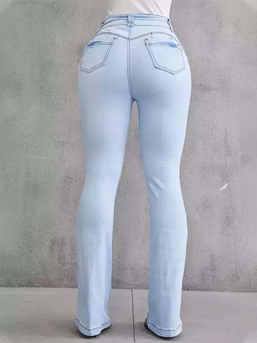 Light blue jeans worn by a person against a gray concrete wall.